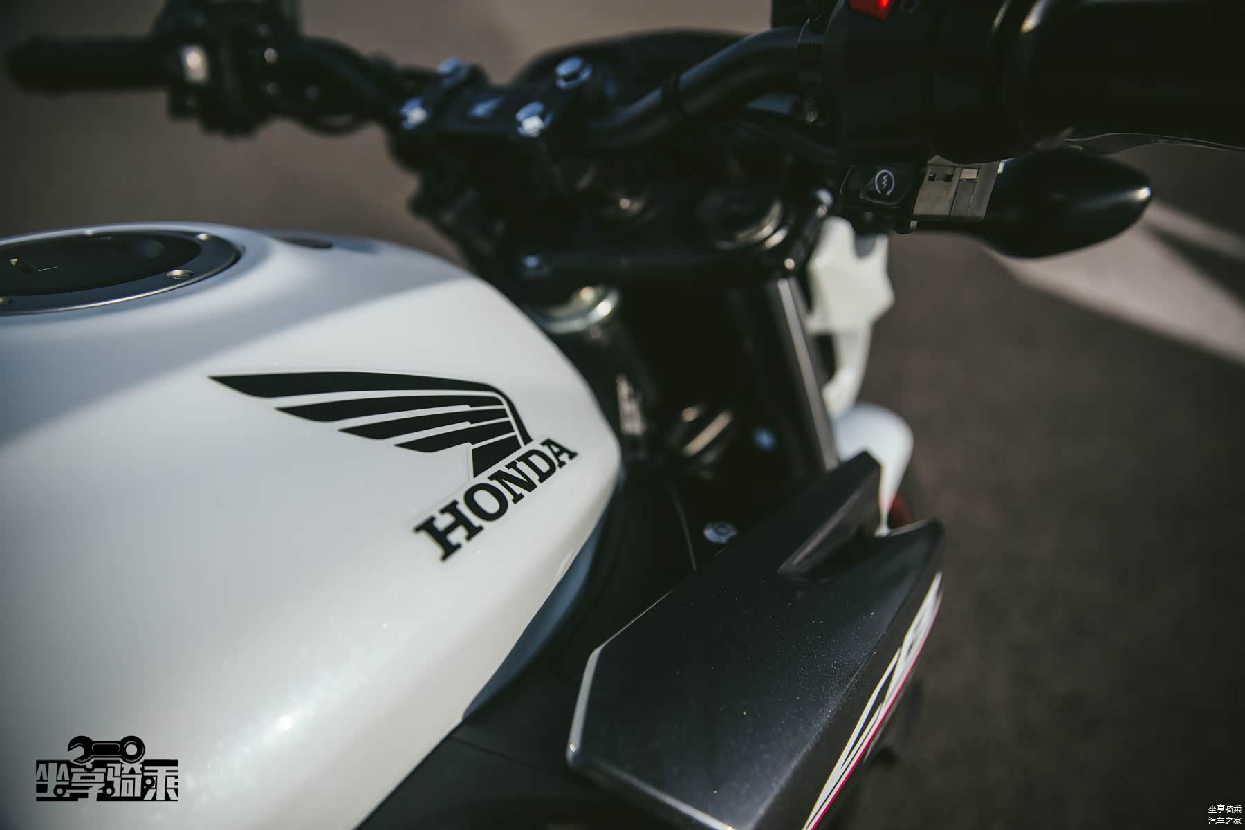 珠光白色车漆在阳光下闪闪发亮，油箱上方印有Honda的鹰翼Logo